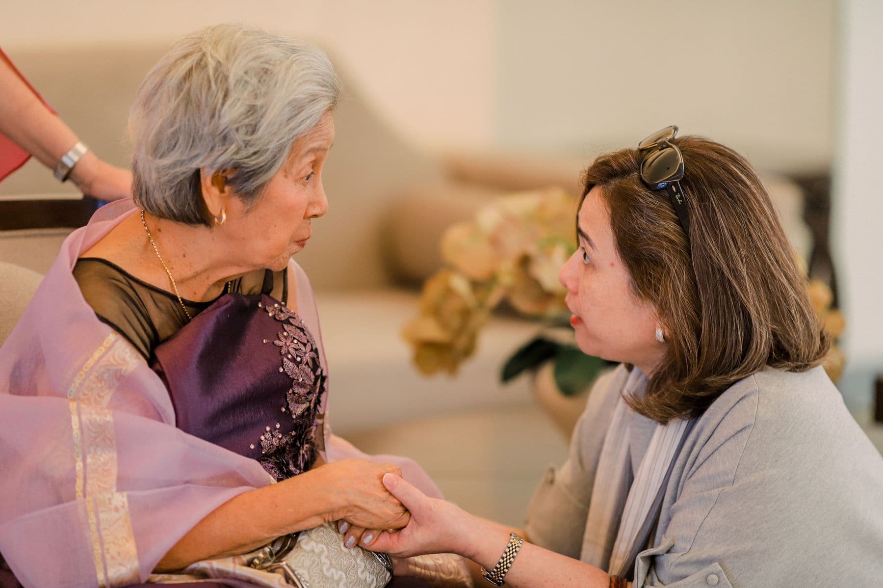 Người phụ nữ châu Á đang trò chuyện và nắm tay một người lớn tuổi.